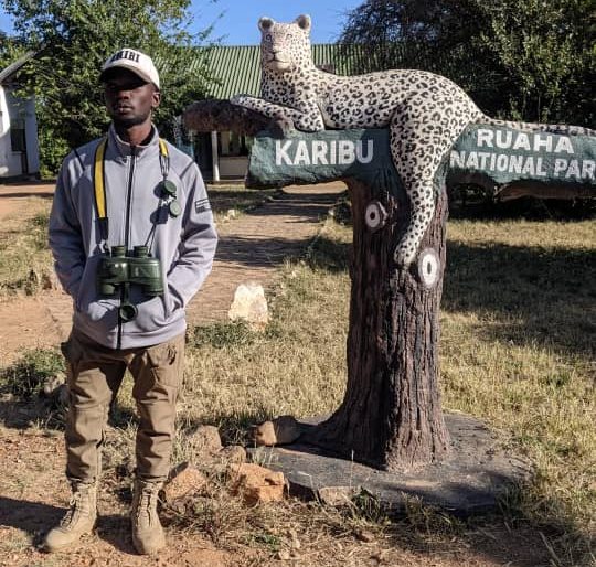 Professional safari guide from Clustered Africa Safaris standing at the Ruaha National Park entrance sign