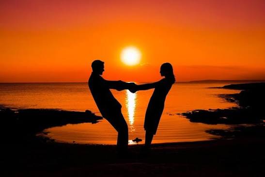 Silhouette of a romantic couple holding hands in a heart shape on the beach at sunset during a Tanzania honeymoon safari.