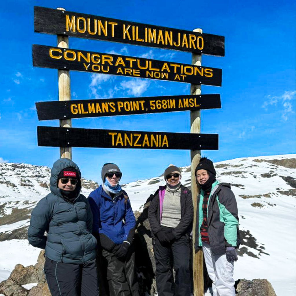 Group of trekkers celebrating at the Mount Kilimanjaro summit signpost during guided tour in Tanzania